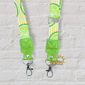 May include: Two lanyards with a lime slice pattern on a yellow and white striped background. The lanyards have bright green leatherette ends with silver-colored swivel hooks. The text "Sunshine Be-Stitched" is visible in the lower right corner.