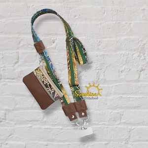 May include: A brown leather wallet with a patterned strap and a white phone holder. The strap has a colorful floral design with green, blue, and yellow accents. The wallet has a zipper and a small pocket.