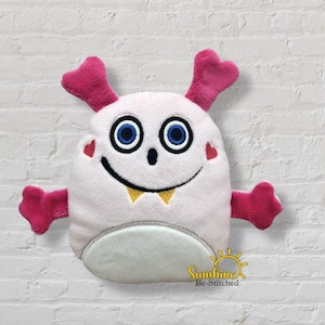 May include: A plush monster toy with a white body, pink horns and arms, and blue eyes. The monster has a smiling face with yellow teeth and red heart-shaped cheeks. The bottom is gray and the toy is embroidered with the text "Sunshine Be-Stitched".