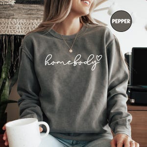 May include: A gray sweatshirt with the text "homebody" in white cursive lettering and a small heart symbol.