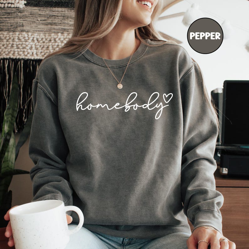 May include: A gray sweatshirt with the text "homebody" in white cursive lettering and a small heart symbol.