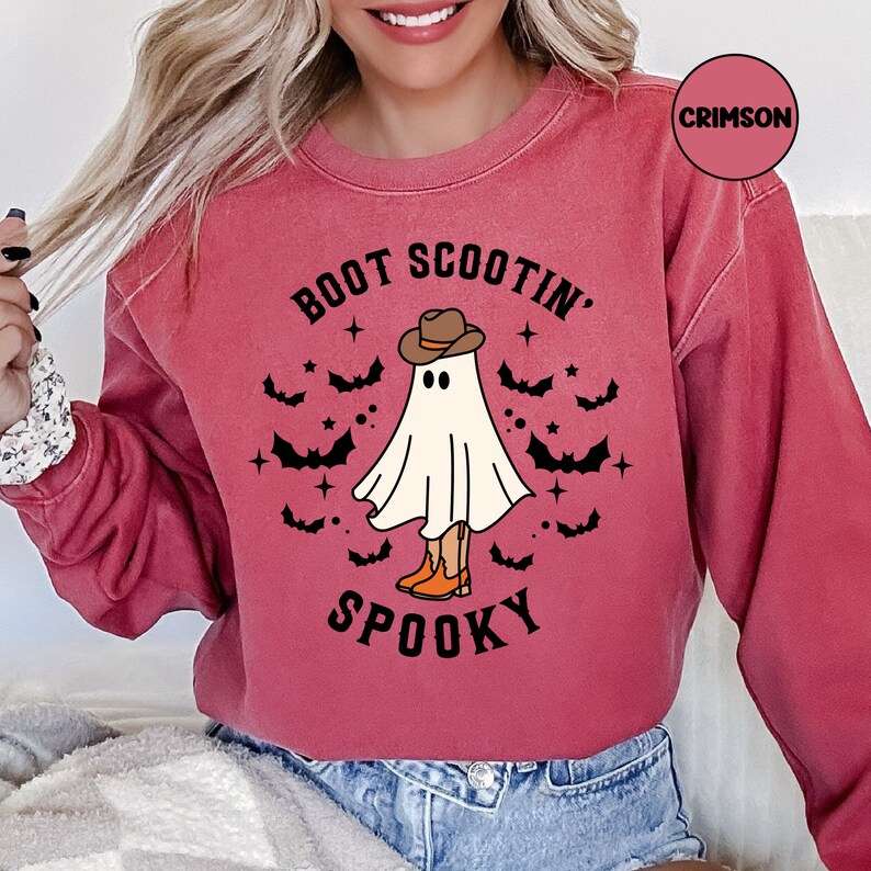 May include: A red sweatshirt with the text "Boot Scootin' Spooky" and a ghost wearing a cowboy hat and boots. The ghost is surrounded by bats and stars.