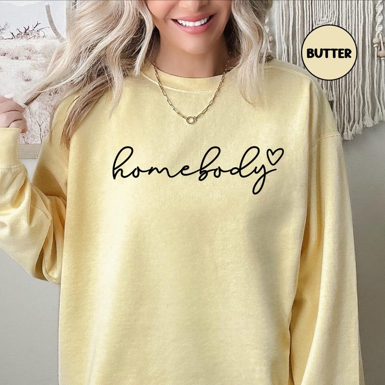 May include: A yellow sweatshirt with the text "homebody" in black script with a small black heart to the right of the word.