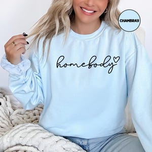 May include: A light blue sweatshirt with the text "homebody" in black cursive lettering and a small heart symbol.