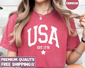 Może przedstawiać: Czerwony t-shirt z białym nadrukiem "USA EST. 1776" z białą gwiazdą pod tekstem.