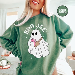 May include: A light green sweatshirt featuring a white ghost holding a pink drink and a brown bag. The text "BOO-JEE" is written in white above the ghost.