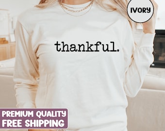 May include: Ivory long-sleeve sweatshirt with the word "thankful" printed in black. The sweatshirt is a neutral color and has a crew neck. The text is in a simple, sans-serif font.