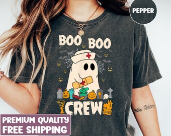May include: A dark gray t-shirt with a ghost wearing a nurse's hat and holding a bandage. The text "Boo Boo Crew" is printed on the shirt with Halloween-themed graphics.