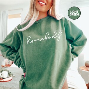 May include: A light green sweatshirt with the text "homebody" in white cursive lettering and a small white heart.
