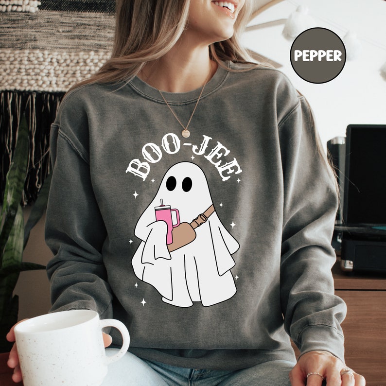 May include: A grey sweatshirt with the text "BOO-JEE" in white and a white ghost holding a pink drink. The ghost is wearing a brown strap across its chest.