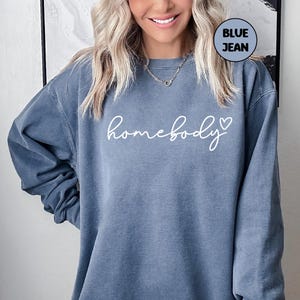 May include: A blue jean sweatshirt with the text "homebody" in white cursive lettering and a small white heart.