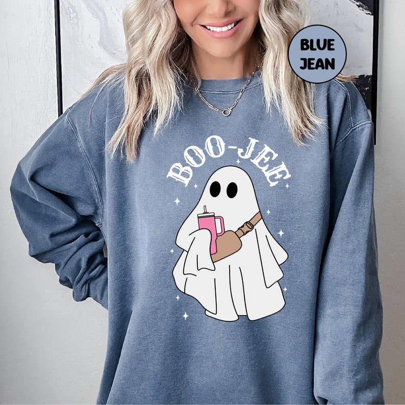 May include: A blue sweatshirt featuring a white ghost graphic holding a pink drink and a brown bag. The text "BOO-JEE" is written in a white outline around the ghost.