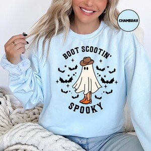 May include: Light blue sweatshirt with a graphic of a ghost wearing a cowboy hat and boots. The text "Boot Scootin' Spooky" is printed on the sweatshirt.