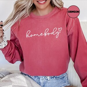 May include: A crimson red sweatshirt with the text "homebody" in white cursive lettering and a small white heart.
