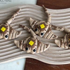 May include: Four brown and tan clay stingray sculptures with yellow accents. The stingrays are arranged on a wavy, light brown surface. The text "CLOUD NINE 3D STUDIO" is visible in the top left corner of the image.