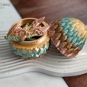 May include: A golden dragon egg trinket box with a detailed dragon head lid. The egg is decorated with a gradient of green, blue, and gold scales.