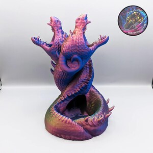 May include: A three-headed dragon sculpture with iridescent purple and blue paint. The dragon is curled up with its heads raised and mouths open. The sculpture is made of plastic and has a textured surface.