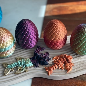 May include: Five iridescent dragon eggs, each with a different color gradient, are arranged on a textured surface.  The eggs are made of a smooth, shiny material and have a scaly texture.  There are also five small dragon figurines, each with a different color and pose.