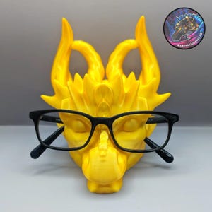 May include: A yellow dragon-shaped glasses holder with a pair of black eyeglasses resting on it.