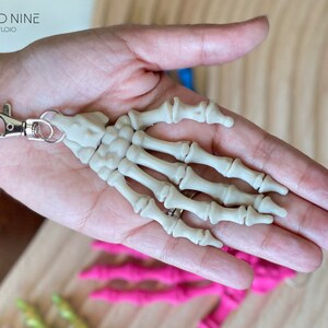 May include: A white plastic skeleton hand keychain with a silver metal clasp.