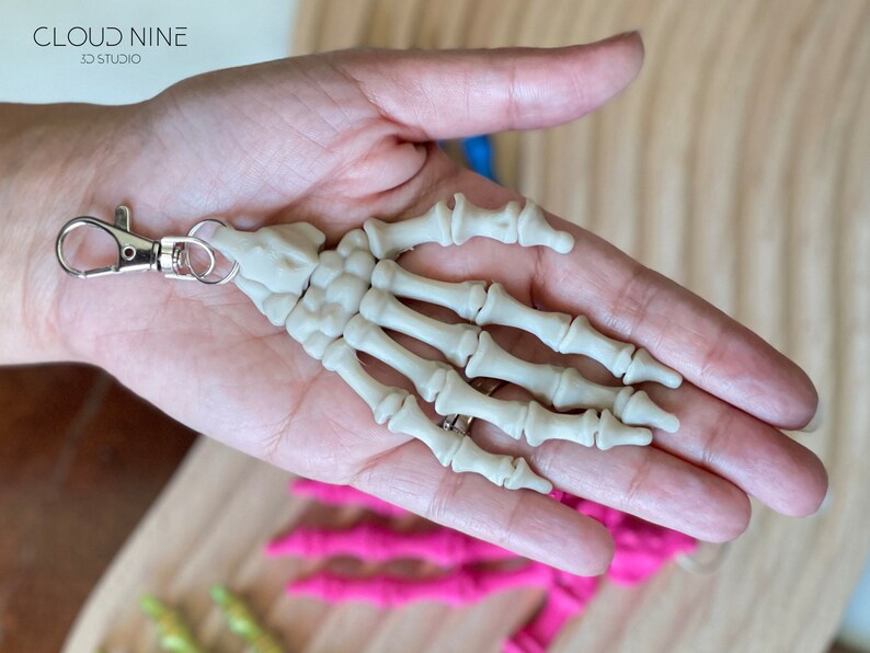 May include: A white plastic skeleton hand keychain with a silver metal clasp.