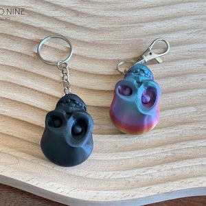 May include: Two skull-shaped keychains, one black and one with a rainbow gradient. Both keychains have silver metal rings.