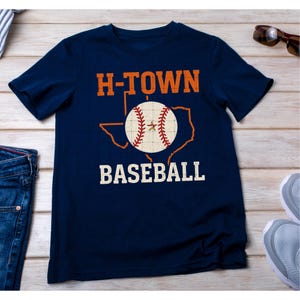 May include: A navy blue t-shirt with a vintage-style graphic of a baseball inside the outline of the state of Texas. The text "H-TOWN BASEBALL" is printed on the shirt.