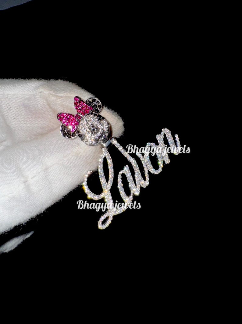 May include: A silver charm necklace with a sparkling diamond-encrusted name "Lavin" and a Mickey Mouse charm with pink bow and black ears. The charm is also covered in sparkling diamonds.