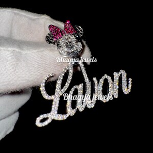 May include: A silver charm necklace with a sparkling diamond-encrusted pendant featuring a Mickey Mouse silhouette with a pink bow and the name "La'Von" spelled out in diamonds.