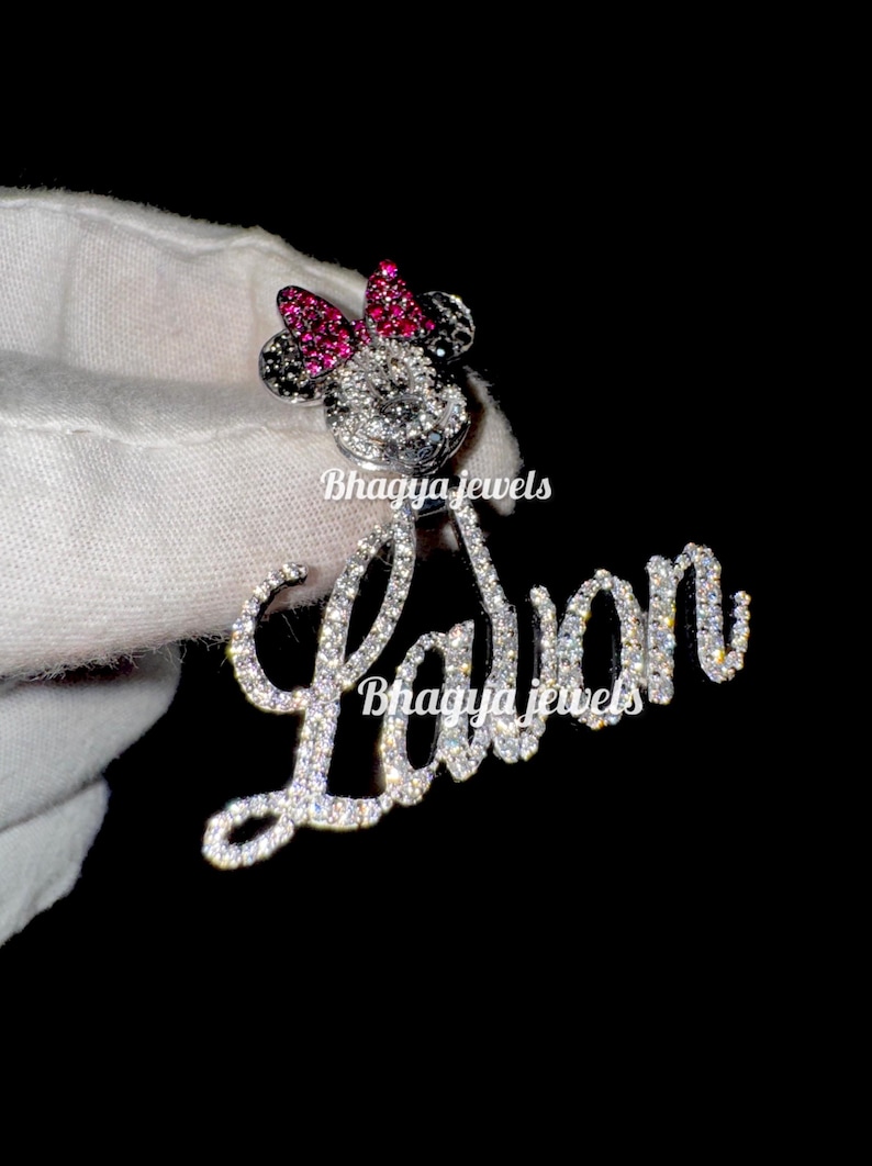 May include: A silver charm necklace with a sparkling diamond-encrusted pendant featuring a Mickey Mouse silhouette with a pink bow and the name "La'Von" spelled out in diamonds.