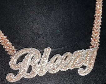 Può includere: Una collana con catena d'oro con un grande ciondolo personalizzato che dice "Blazey" in diamanti scintillanti.