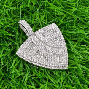 Op de afbeelding: Een zilverkleurige, driehoekige hanger die volledig is bedekt met kleine, sprankelende witte steentjes. De hanger heeft een opvallend oogje aan de bovenkant en de tekst "Bhagya Jewels" staat in kleine, witte letters onderaan gedrukt.