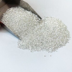 May include: A large scoop filled with loose, white diamonds. The diamonds are scattered on a white surface.