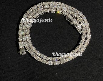 May include: A silver chain necklace with a row of clear, square-shaped stones. The chain is made of metal and has a clasp closure. The necklace is on a black background.