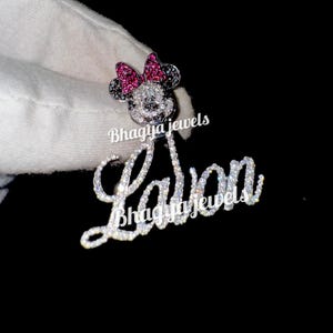 May include: A silver charm necklace with a diamond-encrusted name "Layla" and a Mickey Mouse charm with pink and black accents. The charm is also encrusted with diamonds.