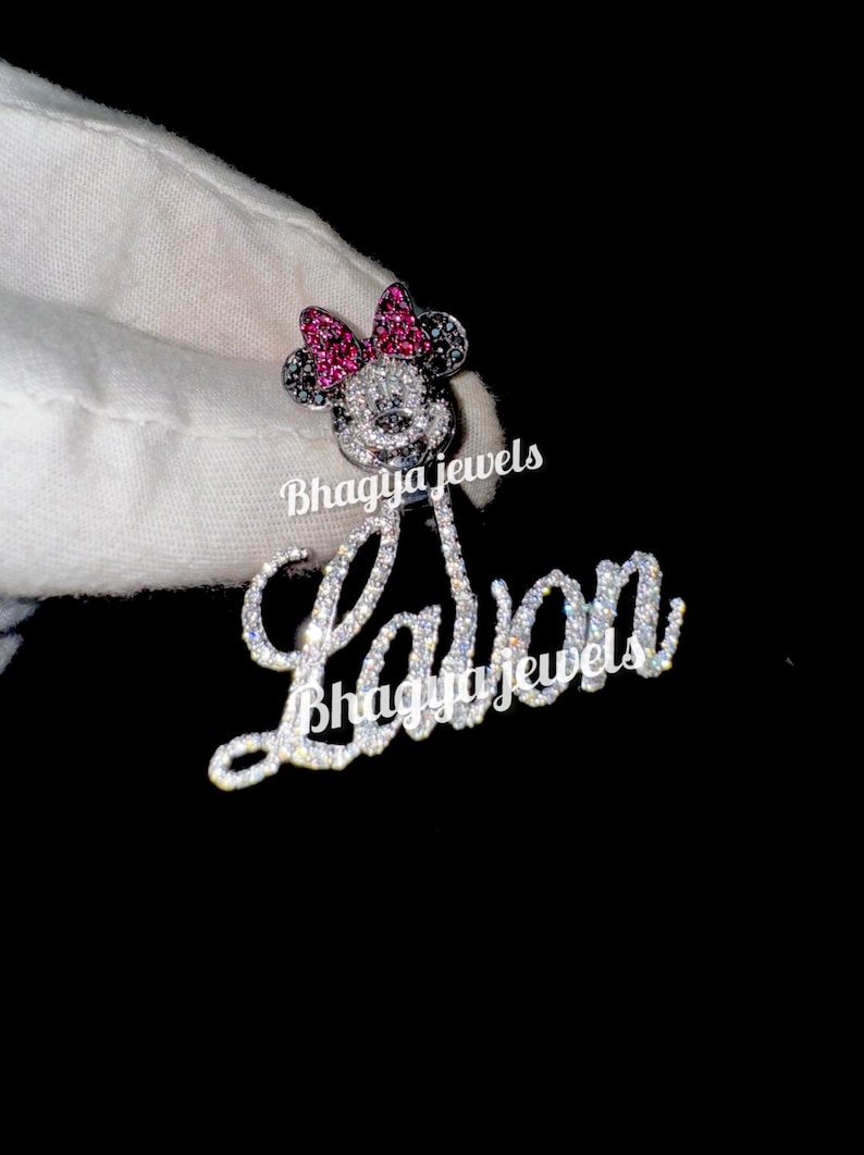 May include: A silver charm necklace with a diamond-encrusted name "Layla" and a Mickey Mouse charm with pink and black accents. The charm is also encrusted with diamonds.