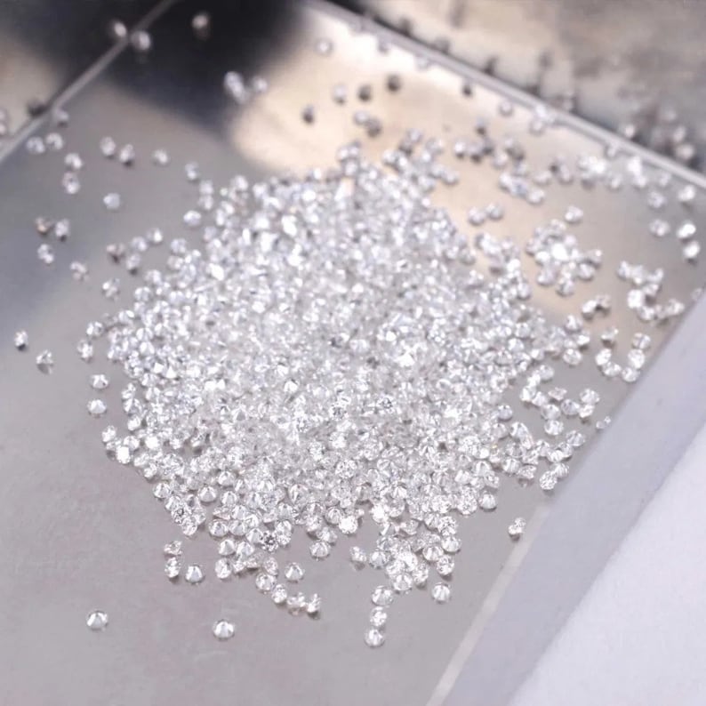 May include: A close-up of a pile of small, clear diamonds on a silver tray.