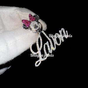 May include: A silver pendant with a custom name "LaVon" spelled out in sparkling rhinestones. The pendant features a small, black and white Mickey Mouse character with a pink bow, also adorned with rhinestones.