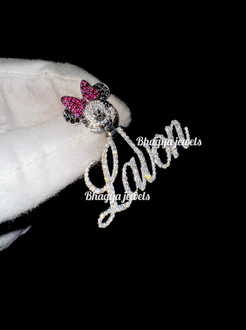 May include: A silver pendant with a custom name "LaVon" spelled out in sparkling rhinestones. The pendant features a small, black and white Mickey Mouse character with a pink bow, also adorned with rhinestones.