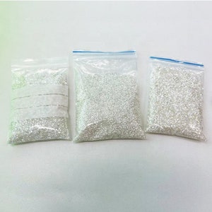 May include: Three clear plastic bags filled with white beads. The bags are sealed with a zipper.