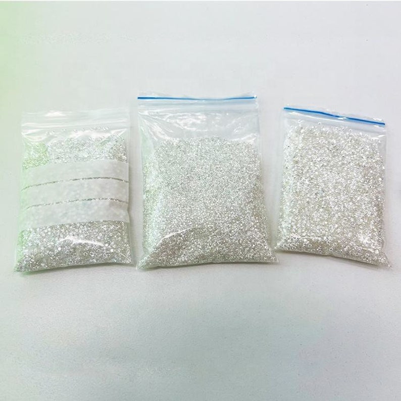 May include: Three clear plastic bags filled with white beads. The bags are sealed with a zipper.