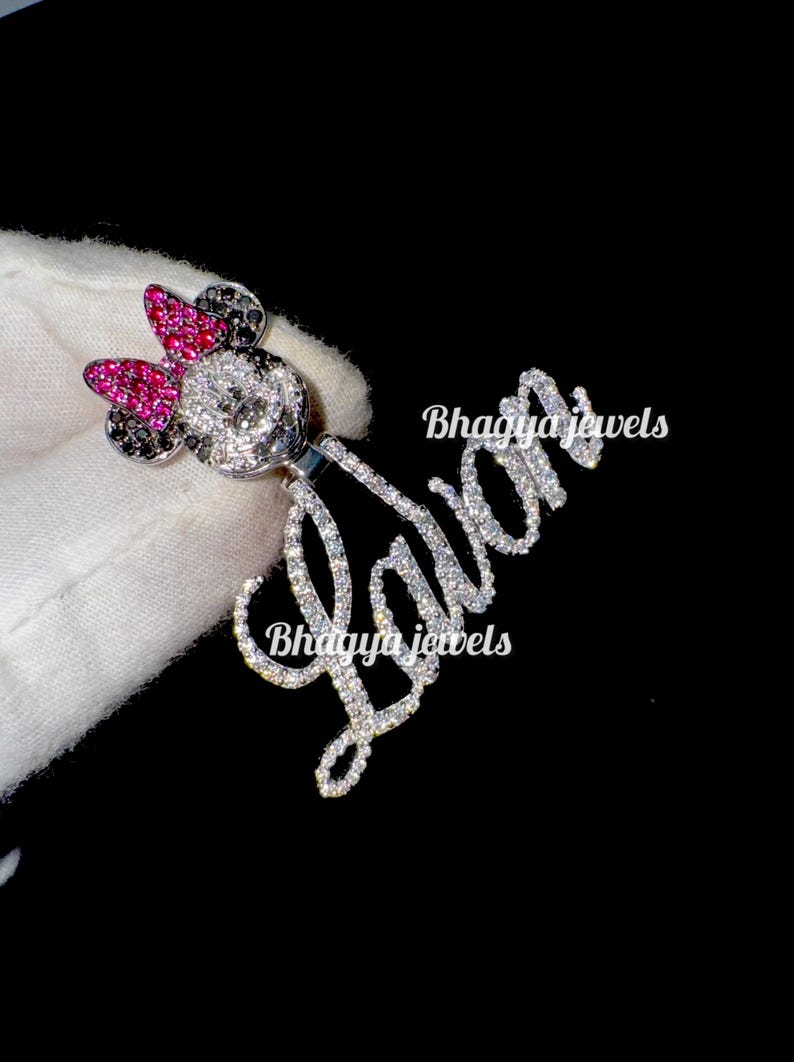 May include: A silver charm necklace with a sparkling diamond-encrusted name "Lavan" and a Minnie Mouse charm with pink and black rhinestones. The charm is attached to a silver chain.