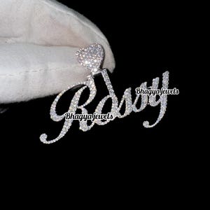 以下が含まれることがあります： 「Roxy」という名前が筆記体で書かれたシルバー製のペンダント。各文字には小さなクリアなキュービックジルコニアが埋め込まれています。ペンダントの上部には、キュービックジルコニアが埋め込まれた小さなハート型のチャームが付いています。