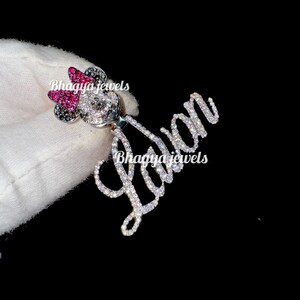 May include: A silver charm necklace with a sparkling diamond-encrusted name "Lavan" and a Mickey Mouse charm with pink and black accents.
