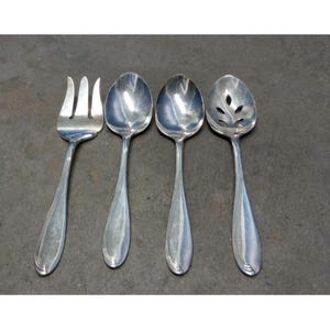 Puede incluir: Se muestran cuatro cubiertos de plata sobre un fondo oscuro. El juego incluye un tenedor, dos cucharas y una cuchara ranurada. Cada pieza tiene un mango largo y delgado con un diseño decorativo cerca de la base.