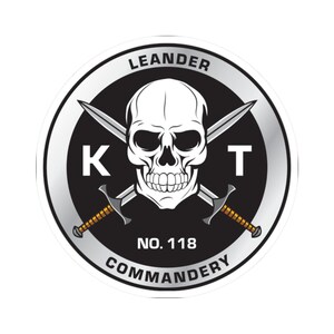 May include: A circular sticker with a skull and crossed swords design. The text includes "LEANDER," "K," "T," "NO. 118," and "COMMANDERY." The colour scheme is black, silver, and white. The skull has detailed features.