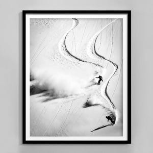 Könnte beinhalten: Schwarzweißfoto von zwei Skifahrern, die in frischem Pulverschnee auf einer schneebedeckten Bergabfahrt Kurven fahren.