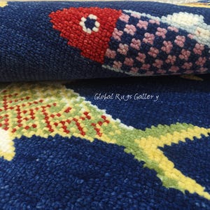 Könnte beinhalten: Nahaufnahme eines aufgerollten blauen Teppichs mit Fischmuster. Die Fische haben rote, rosa, gelbe und grüne Details. Die Textur des Teppichs ist sichtbar, und die Worte "Global Rugs Gallery" sind im Bild.