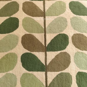 May include: Close-up of a rug featuring a repeating leaf design. The leaves are in various shades of green and brown, set against a cream backdrop. A dark brown vertical line runs through the centre.