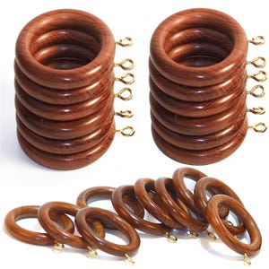 Puede incluir: Un conjunto de anillas circulares para cortinas hechas de madera marrón pulida con vetas visibles. Cada anilla cuenta con un pequeño ojal de metal dorado fijado en el borde exterior para colgar. El set incluye dos pilas verticales y una fila.